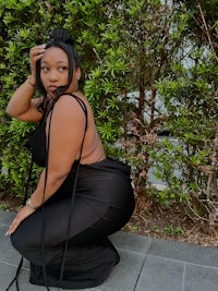 a woman in a black dress crouching in front of bushes